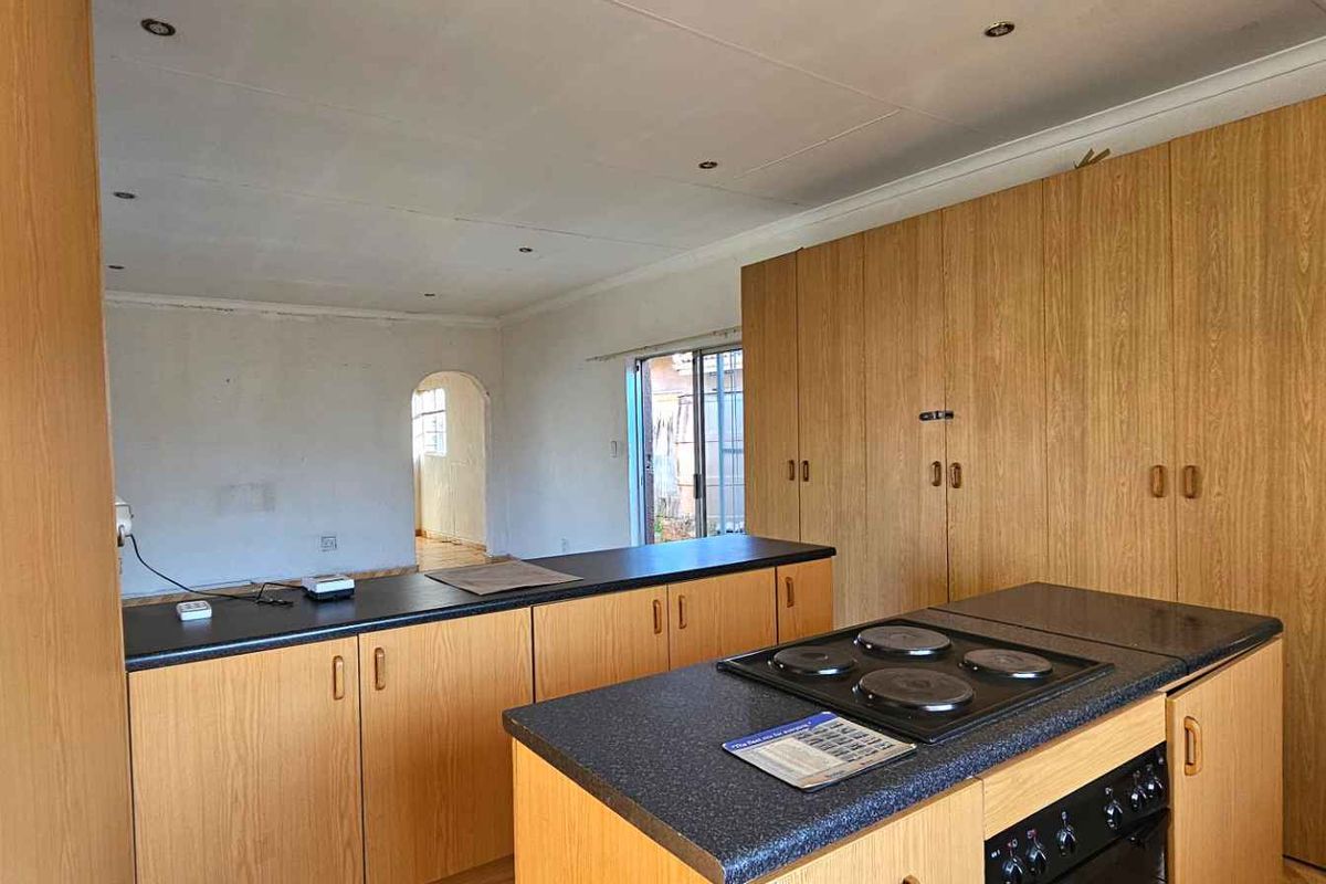 A functional kitchen featuring extensive wood-veneer cabinetry, a central island with a built-in electric hob and oven, and dark laminate countertops.
