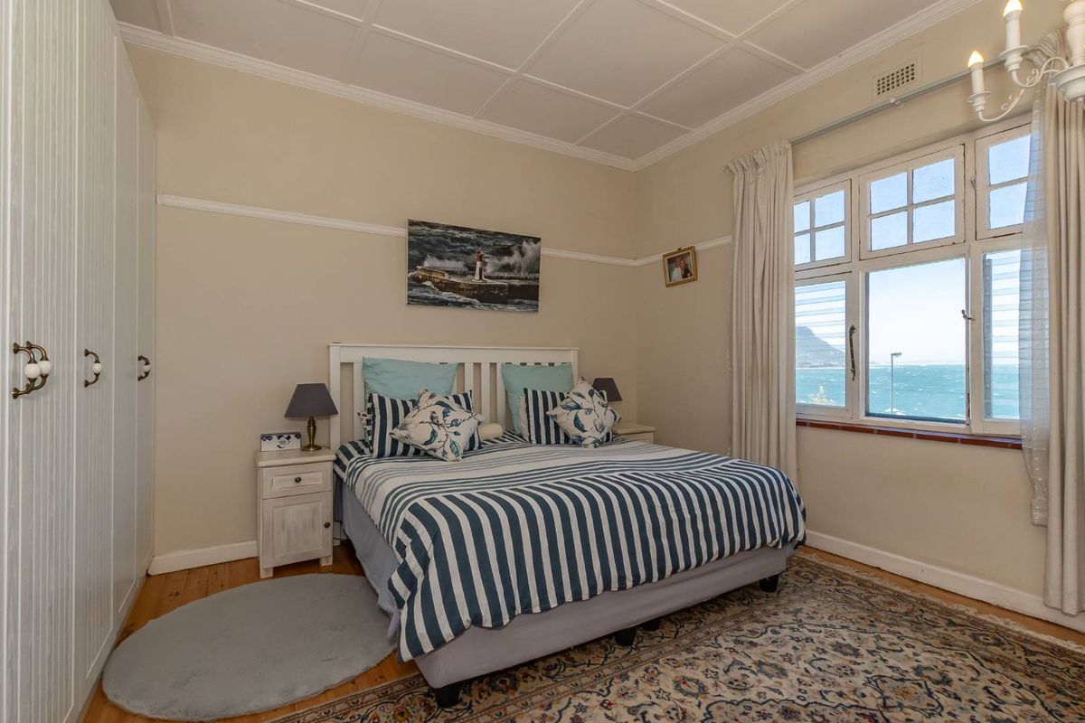 A well-maintained bedroom featuring timber flooring, built-in wardrobes, and a large window offering scenic coastal views.
