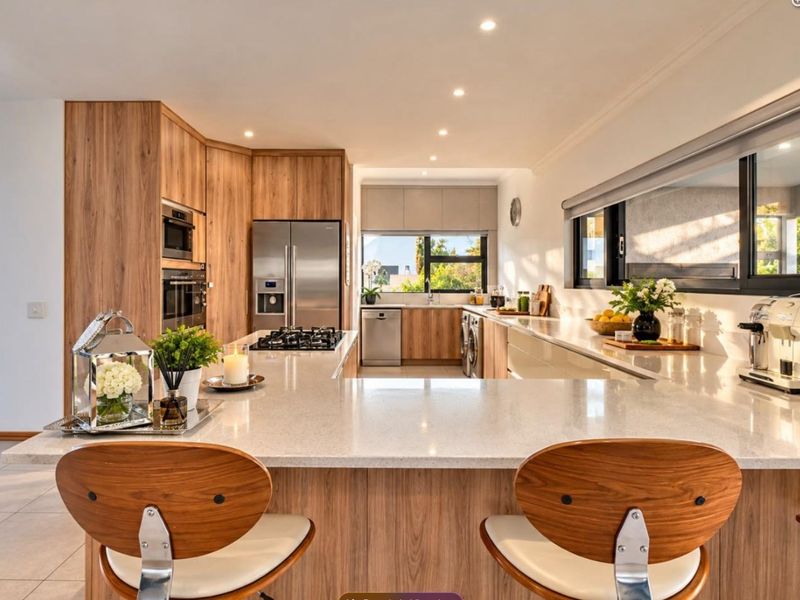 Modern, well-appointed kitchen featuring wood-grain cabinetry, stone countertops, high-end built-in appliances, and a spacious breakfast bar island.