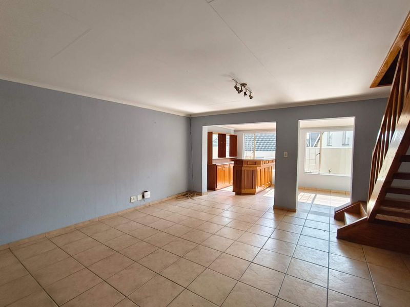 Spacious open-plan living area featuring tiled flooring, a built-in wooden bar, and a staircase leading to the upper level.