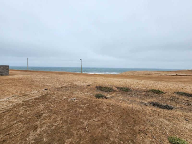 A wide-angle view of a vacant residential plot featuring an unpaved road, street lighting, and direct ocean views.
