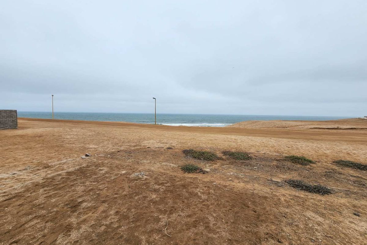 A wide-angle view of a vacant residential plot featuring an unpaved road, street lighting, and direct ocean views.
