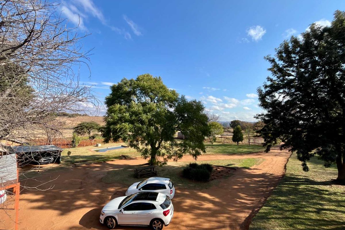 An elevated view of the farm grounds featuring a large open garden area, mature trees, and a dirt driveway.