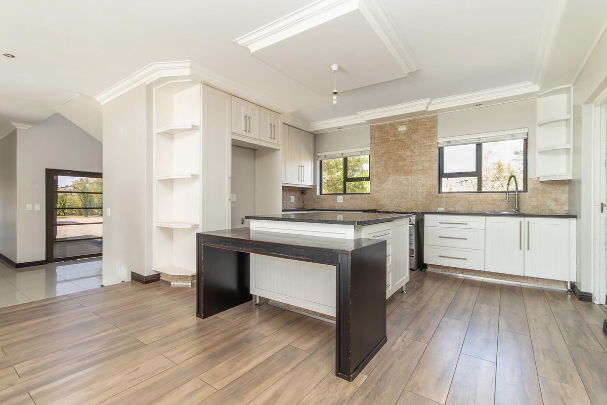 Modern kitchen featuring white cabinetry, granite countertops, a central island with breakfast bar, and wood-look tile flooring.