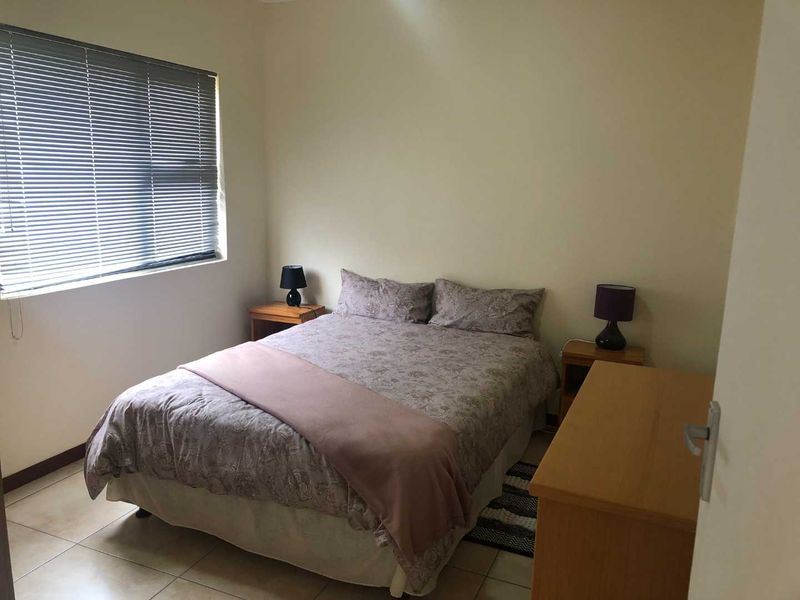 A functional bedroom featuring neutral wall tones, tiled flooring, and a window fitted with venetian blinds.