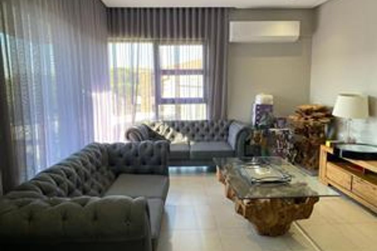 A well-lit living room featuring tiled flooring, recessed downlighting, a wall-mounted split-system air conditioner, and large sliding glass doors with floor-to-ceiling curtains.