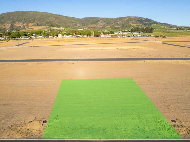 Aerial view of a cleared residential plot in a developing estate, featuring road access and mountain views.