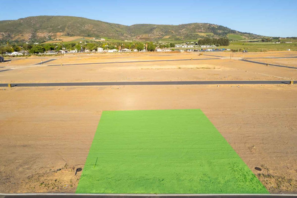 Aerial view of a cleared residential plot in a developing estate, featuring road access and mountain views.