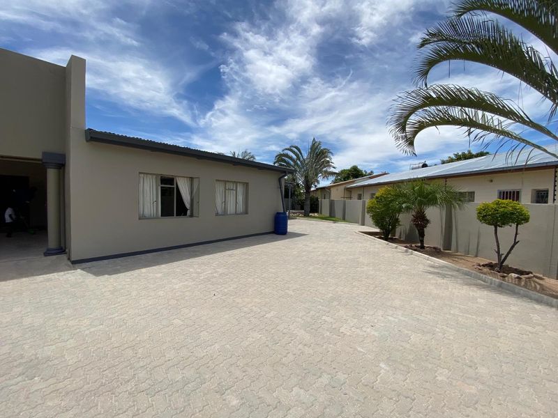 A clean front exterior view featuring a spacious paved driveway, boundary walls, and well-maintained building facade under a clear sky.