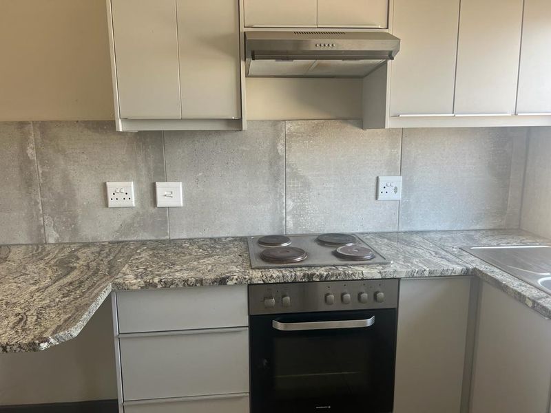 A functional kitchen featuring granite countertops, built-in cabinetry, an electric hob, oven, and extractor fan with a neutral tiled backsplash.