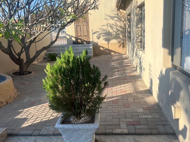 A paved outdoor patio area featuring tiled flooring, exterior wall access, and a landscaped garden setting.