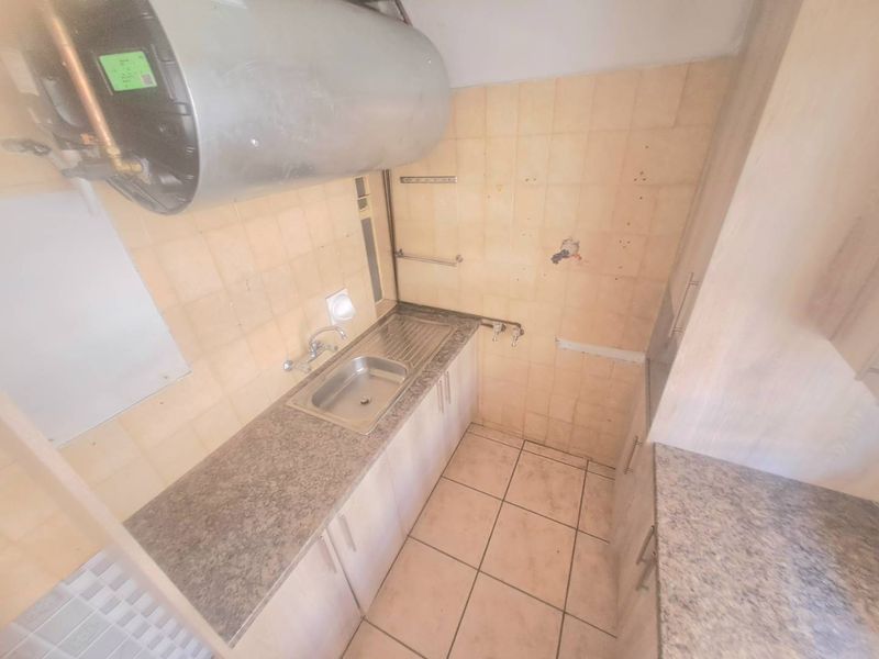 A compact, dated kitchen area featuring a stainless steel sink, laminate countertops, and tiled finishes, currently in need of renovation and modernization.