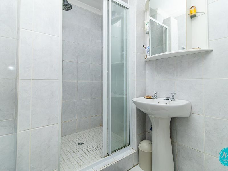 A functional bathroom featuring a pedestal basin, a shower enclosure with tiled walls, and a wall-mounted medicine cabinet.