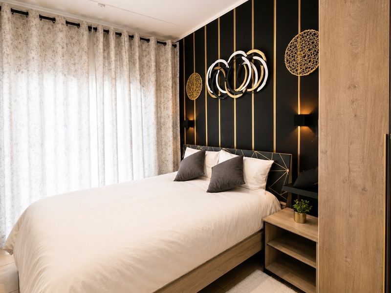 A modern, well-appointed bedroom featuring a built-in wardrobe, stylish accent wall with integrated lighting, and neutral tiled flooring.