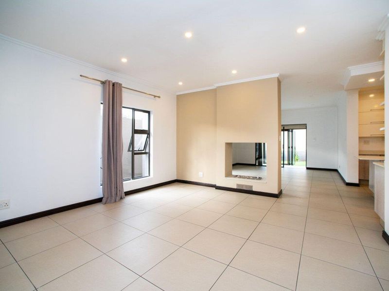 Spacious open-plan living area featuring neutral tiled flooring, recessed downlights, and a central built-in fireplace, flowing seamlessly into the adjacent kitchen space.
