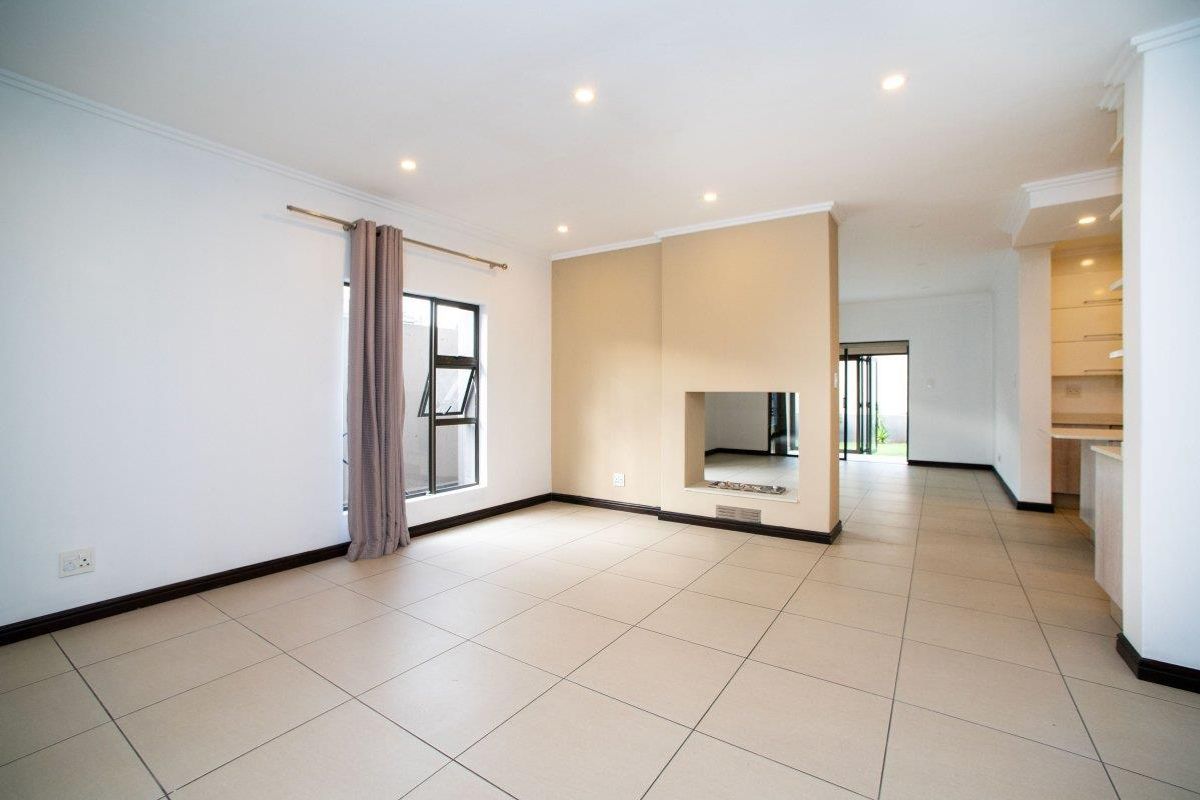 Spacious open-plan living area featuring neutral tiled flooring, recessed downlights, and a central built-in fireplace, flowing seamlessly into the adjacent kitchen space.