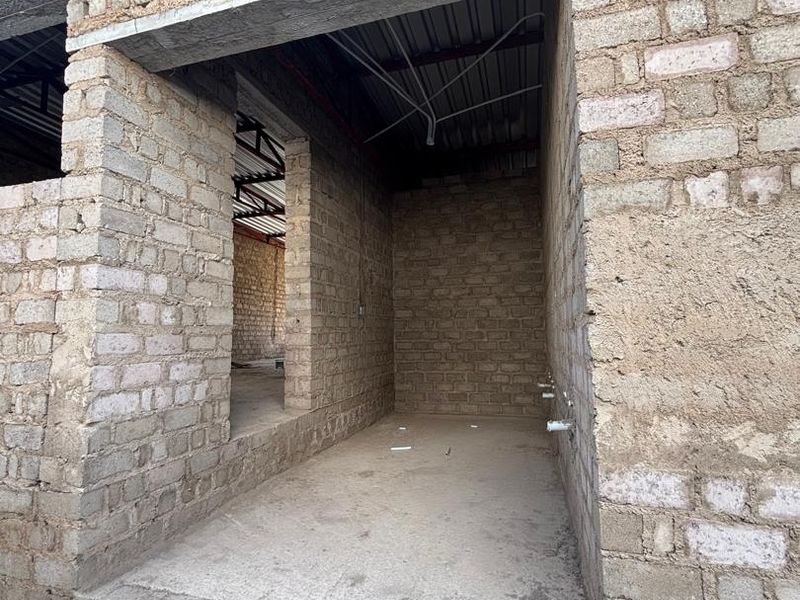 An unfinished utility space under construction, featuring exposed brick walls, concrete flooring, and visible plumbing rough-ins, awaiting final finishes and installation.