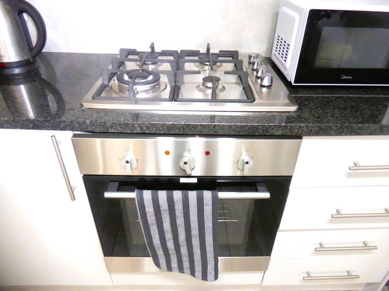 A clean kitchen area featuring a stainless steel gas cooktop, built-in oven, and dark granite countertops with white cabinetry.
