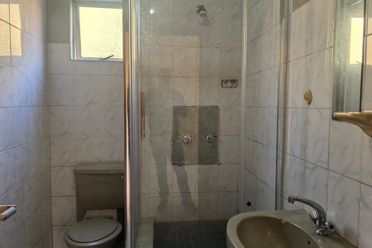 A dated bathroom featuring a shower enclosure, toilet, and pedestal basin with tiled finishes, currently requiring maintenance and cosmetic updates.