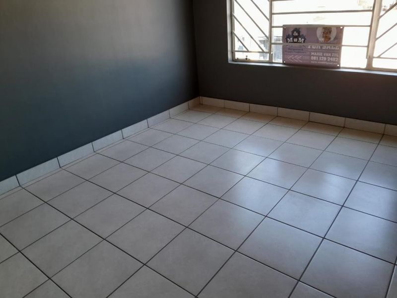An empty bedroom featuring neutral tiled flooring, dark grey walls, and window security bars.