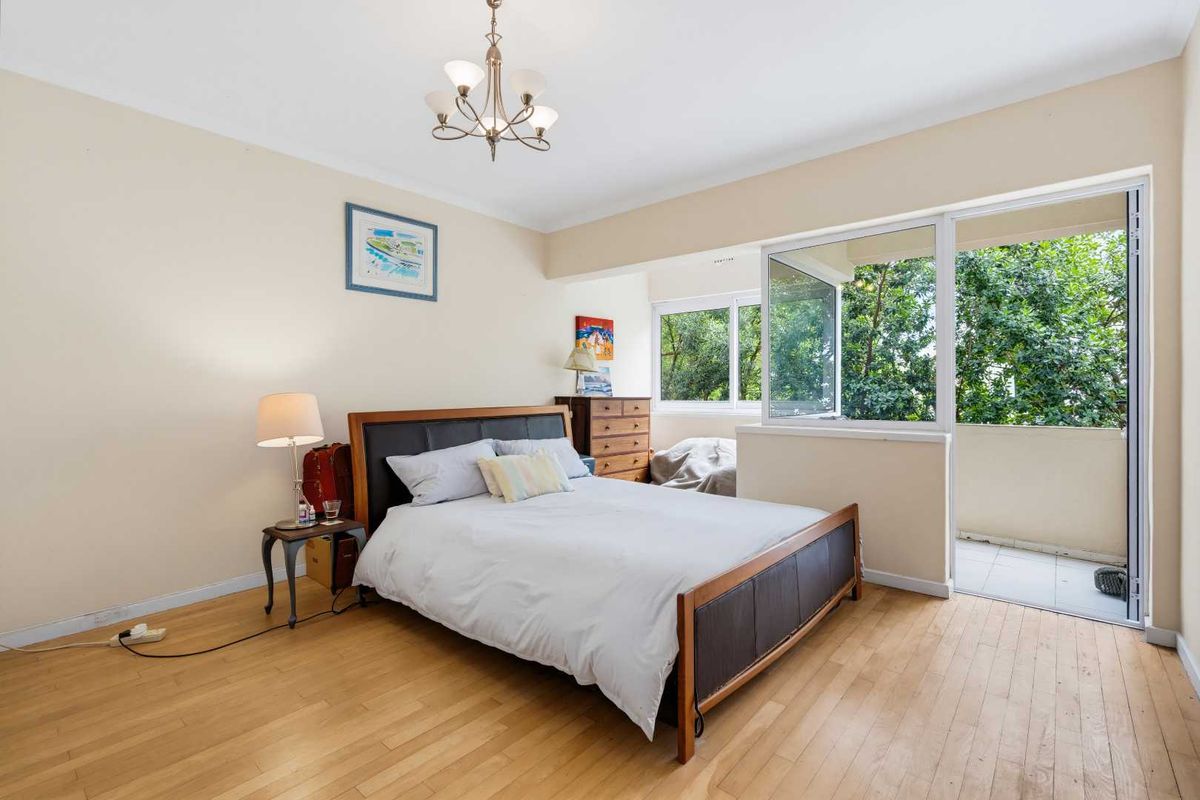 Spacious bedroom featuring hardwood flooring and direct access to a private balcony through sliding glass doors, providing ample natural light.
