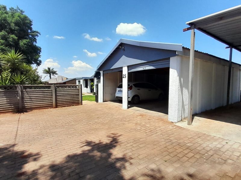 Exterior view of a residential property featuring a paved driveway, a single garage, and an adjacent carport structure.