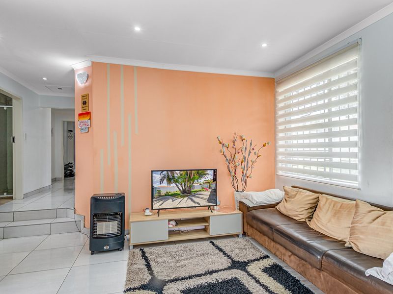 A bright living room featuring tiled flooring, recessed downlighting, and a feature wall, providing a functional and well-lit space.