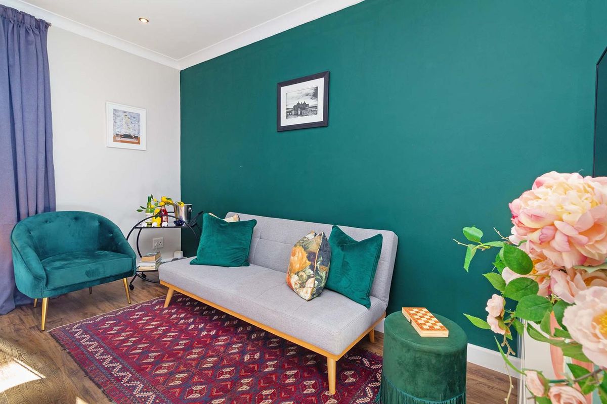 A well-maintained living room featuring a bold green accent wall, recessed downlighting, and durable laminate flooring.