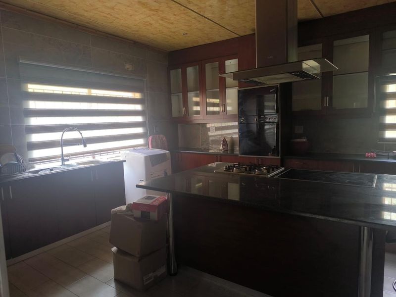 A functional kitchen featuring dark wood cabinetry, granite countertops, a gas hob with extractor fan, and tiled finishes throughout.