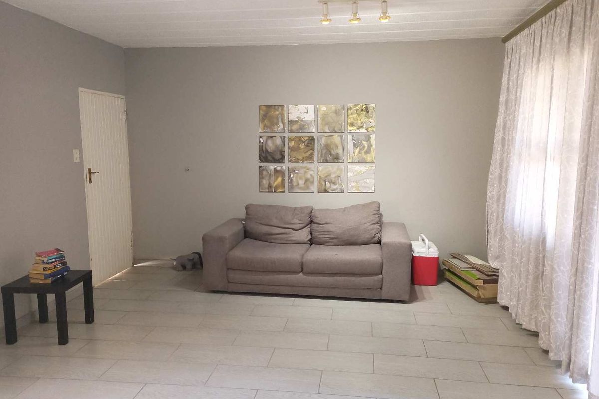 A neutrally painted living room featuring light-colored floor tiles, a panel door, and ceiling-mounted track lighting.