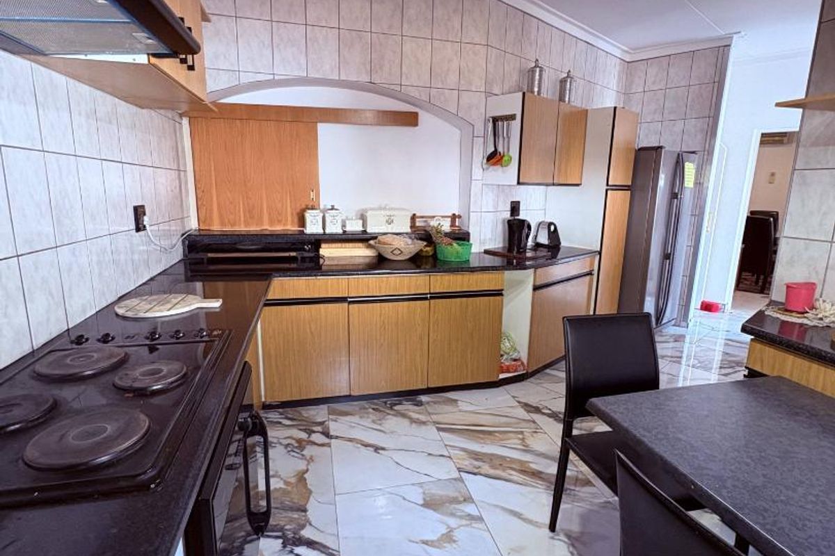A functional kitchen featuring wood-finish cabinetry, dark countertops, a built-in electric hob with extractor, and distinctive marble-patterned floor tiles.