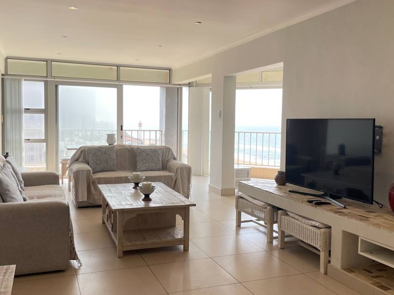 Spacious open-plan living area featuring tiled floors, recessed lighting, and large sliding glass doors that open onto a balcony with ocean views.
