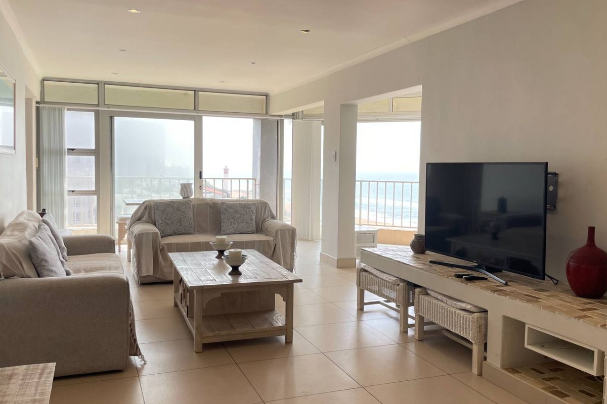 Spacious open-plan living area featuring tiled floors, recessed lighting, and large sliding glass doors that open onto a balcony with ocean views.