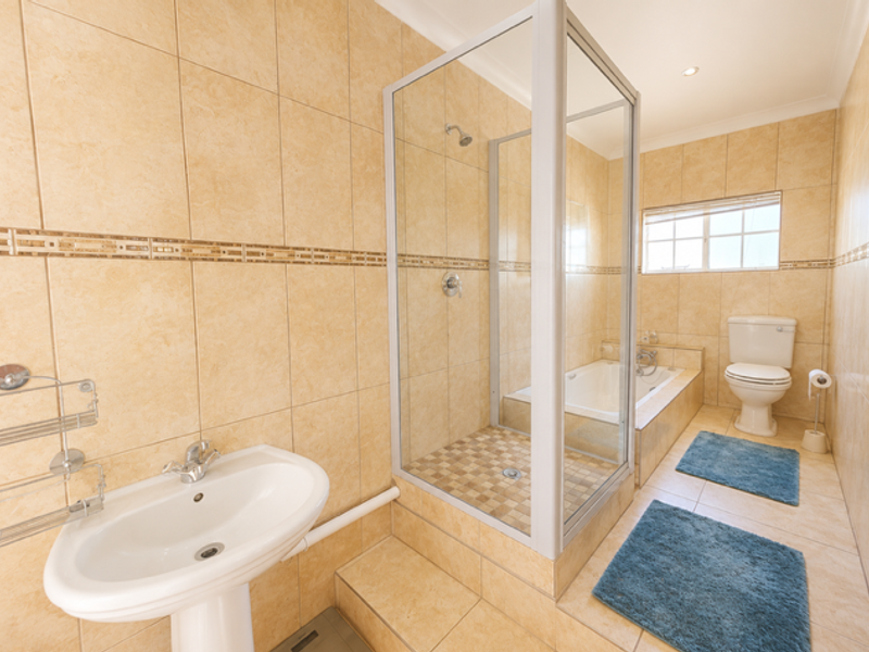A well-maintained bathroom featuring a pedestal basin, a separate shower enclosure, a built-in bathtub, and a toilet, finished with neutral floor-to-ceiling tiling.