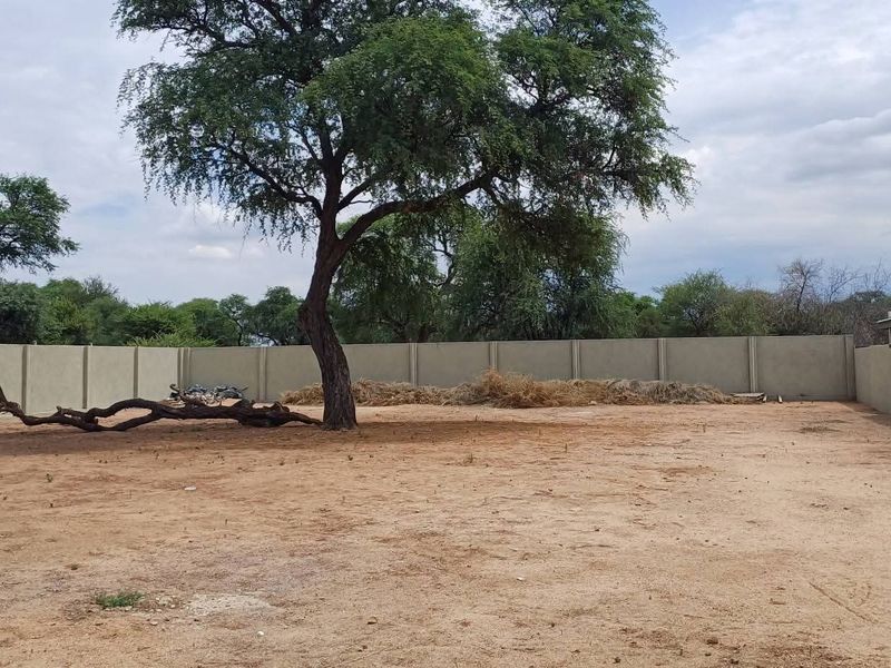 A vacant residential plot featuring a mature tree and enclosed by a precast concrete boundary wall.