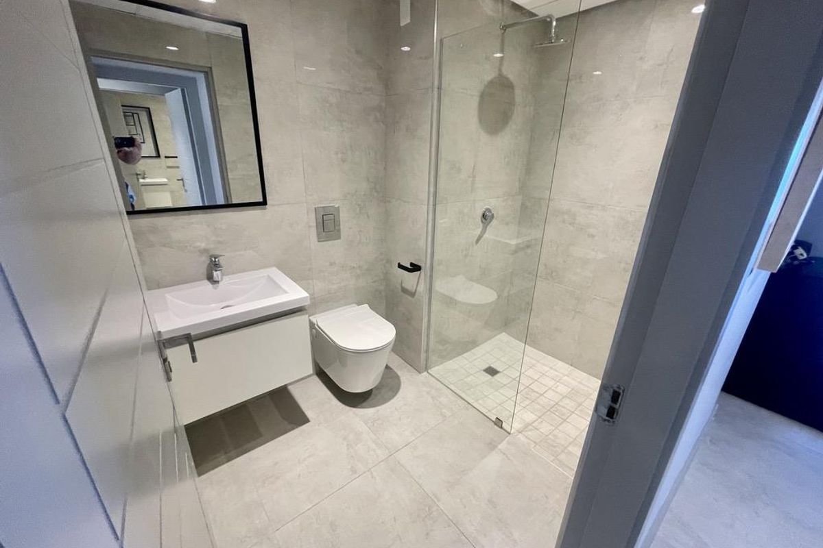 Modern bathroom featuring a wall-mounted vanity, a frameless glass walk-in shower, and a concealed cistern toilet with neutral floor-to-ceiling tiling.
