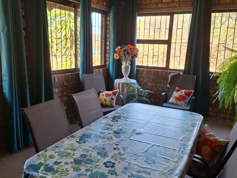 A dining area featuring exposed brick walls, large windows with security bars, and tiled flooring, providing a rustic and well-lit space for meals.