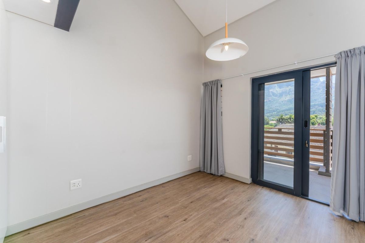 A bright, empty bedroom featuring wood-look flooring, high ceilings, and a glass sliding door leading to a private balcony with mountain views.