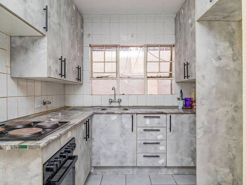 Compact kitchen featuring grey-toned cabinetry, built-in electric oven and hob, tiled backsplash, and a functional sink area with window view.