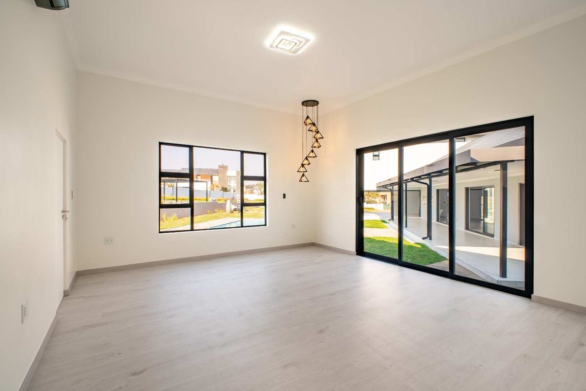 A bright, modern living area featuring light wood-look flooring, large black-framed sliding doors leading to a patio, and contemporary pendant lighting.