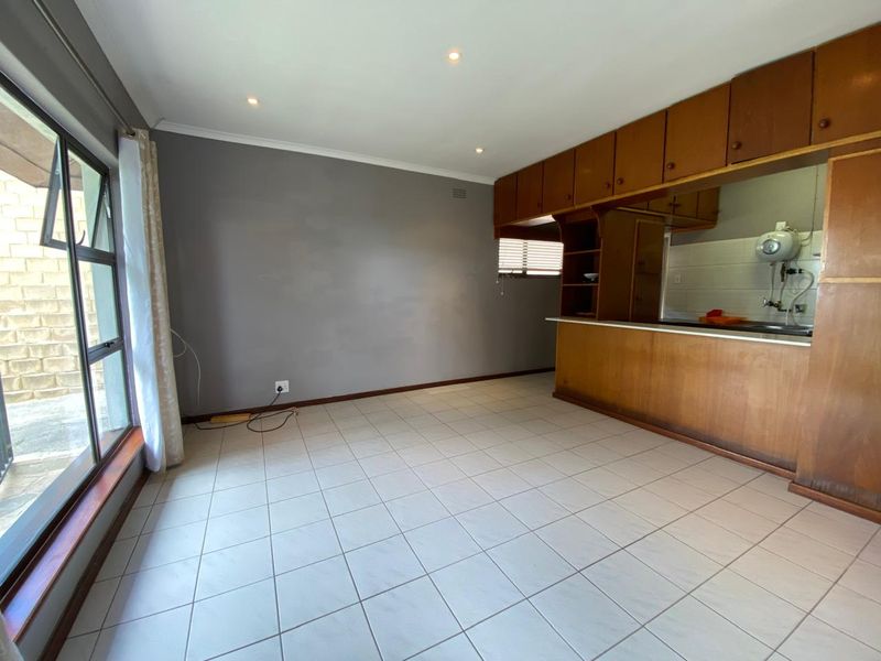 Open-plan living area featuring tiled flooring, recessed lighting, and a built-in wooden kitchen counter with overhead cabinetry.