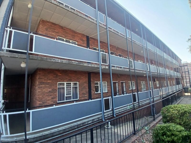 Exterior view of a multi-story apartment building featuring a brick facade, external walkways, and metal balcony railings.