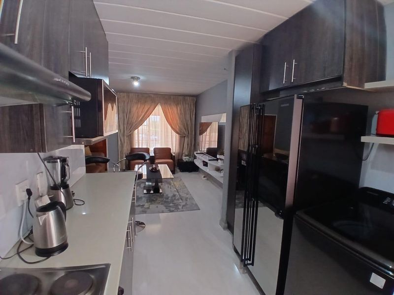 An open-plan kitchen and living area featuring modern dark cabinetry, integrated shelving, and tiled flooring, creating a functional and cohesive living space.