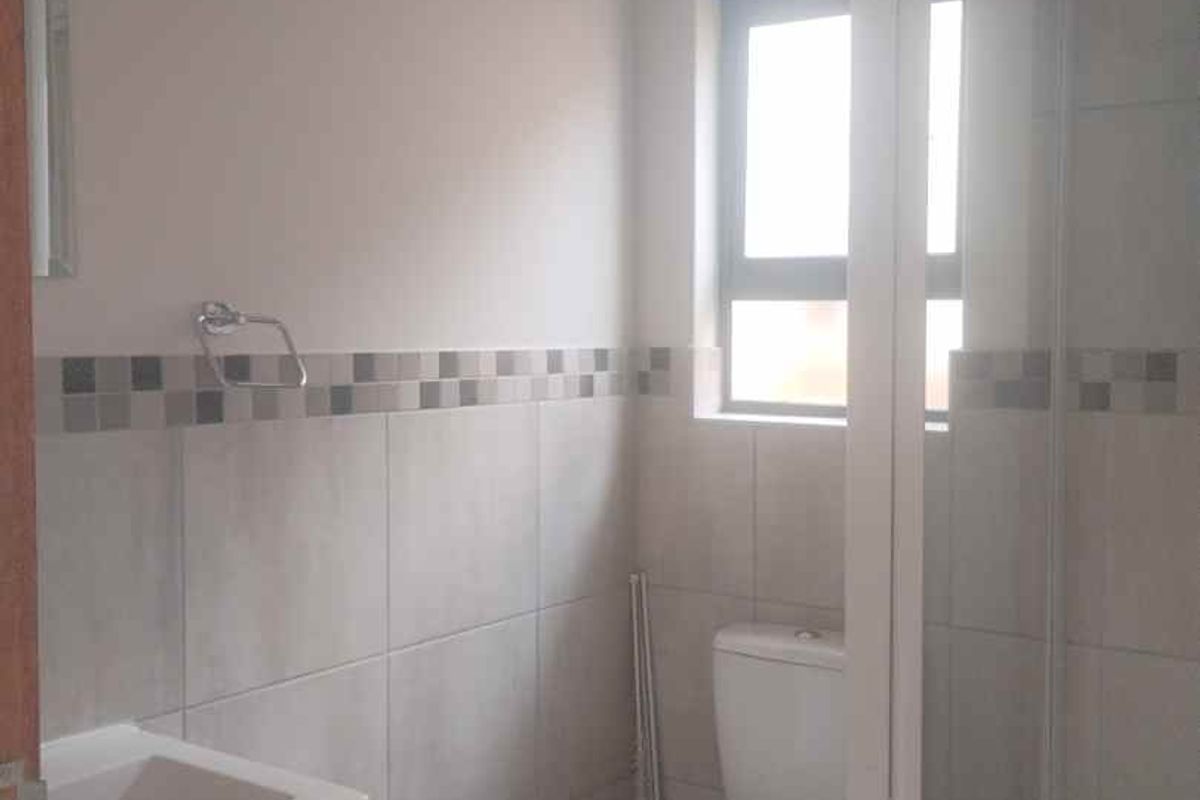 A clean, functional bathroom featuring a shower enclosure, toilet, and vanity basin with neutral wall and floor tiling.