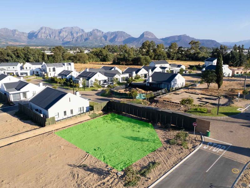 An aerial view of a vacant residential plot in a developed estate, featuring clear road access and scenic mountain views.