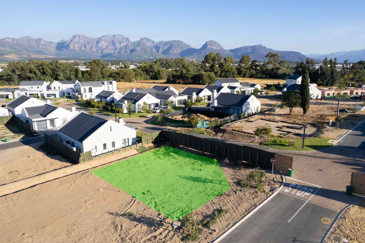 An aerial view of a vacant residential plot in a developed estate, featuring clear road access and scenic mountain views.