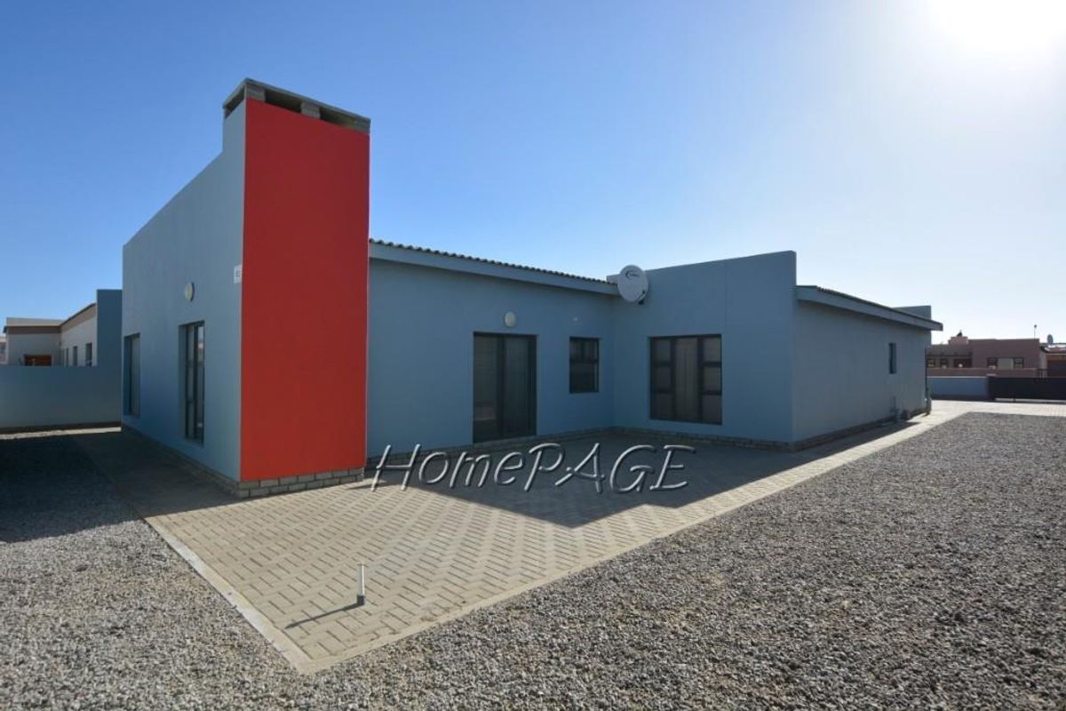 Rear view of a modern house featuring a distinctive red chimney stack, paved patio area, and gravel landscaping.