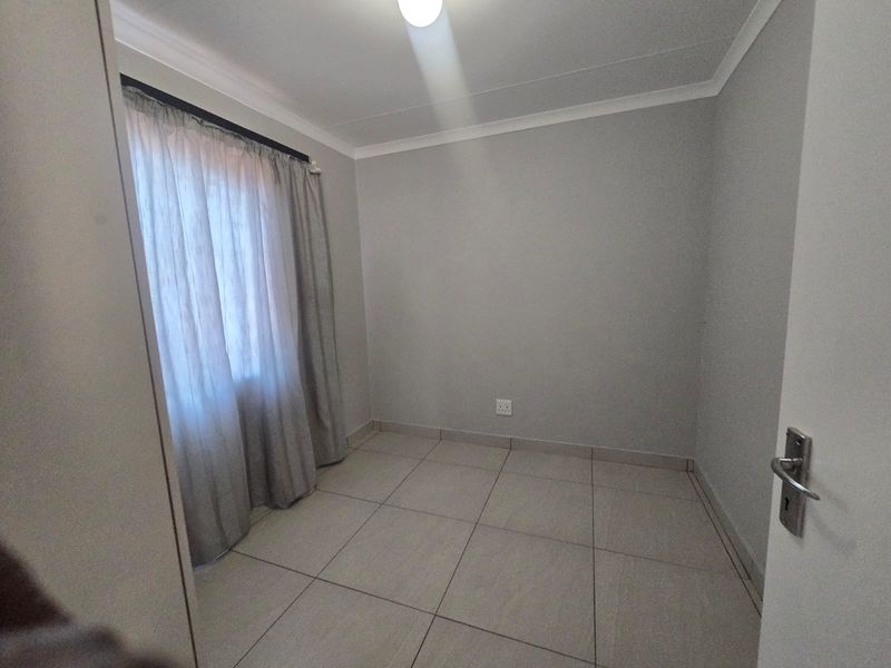 A clean, empty bedroom featuring neutral tiled flooring, coved ceilings, and a window with curtains, providing a versatile space ready for furnishing.