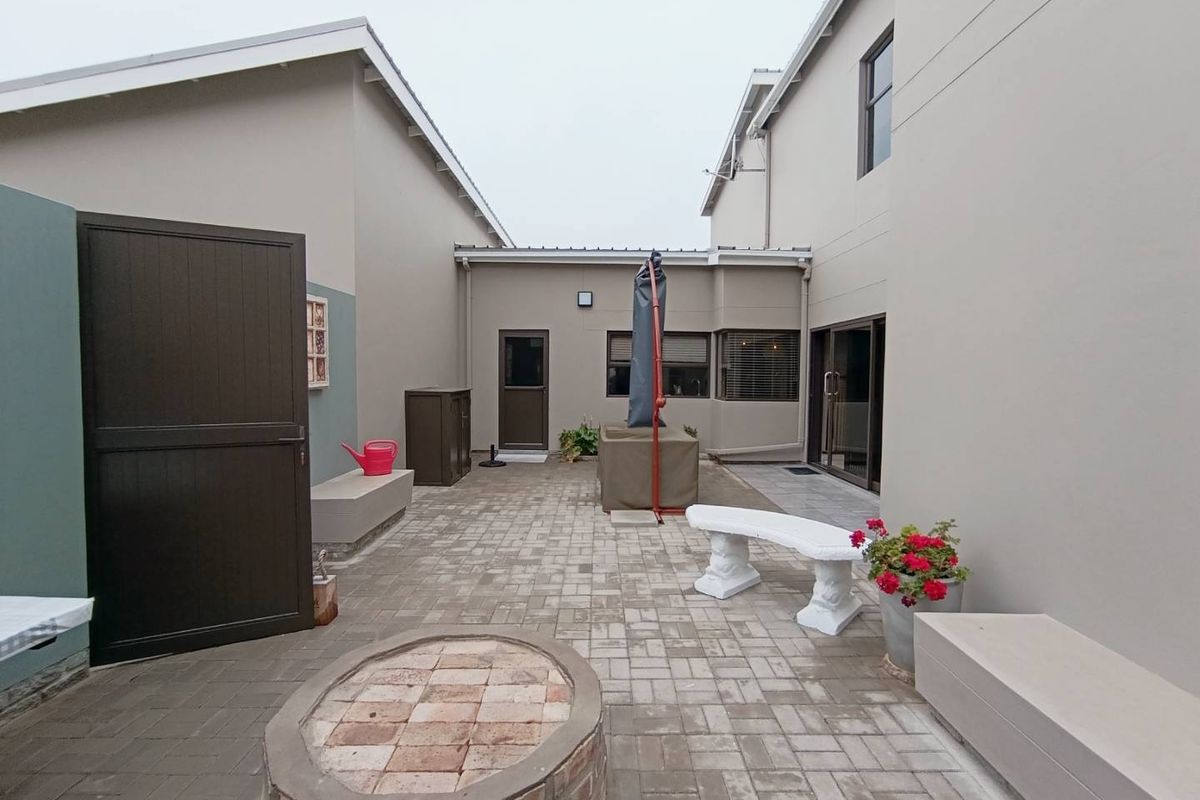 A well-maintained paved rear courtyard featuring a built-in brick fire pit, concrete bench seating, and direct access to the home via sliding glass doors.