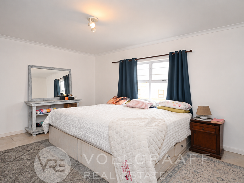 A well-lit bedroom featuring tiled flooring, neutral walls, and a window with dark curtains, providing a comfortable and functional sleeping space.
